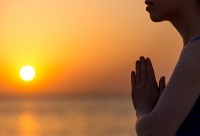 Profile of serene young woman relaxing on the beach meditating with hands in Namaste gesture at sunset or sunrise close up